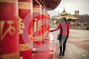 Photo of young beautiful woman turning red prayer wheels in buddhist temple.