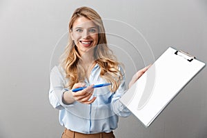 Photo of young blond secretary woman with long curly hair writing down notes in clipboard while working in office