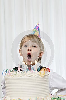 Portrait of young boy wearing party hat blowing candles on birthday cake