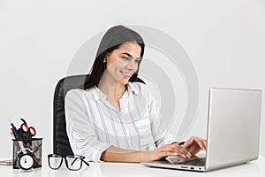 Photo of young brunette businesswoman working on laptop in office isolated over white background