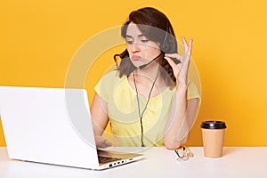 Photo of young brunette woman, assistant in business centre gives consultation to client via video call, lady sitting with headset