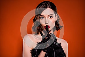 Photo of young charming glamour woman hold finger red lips mute silence witch isolated on dark orange color background