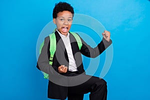 Photo of young cheerful dark skin happy small boy winner celebrate wear backpack isolated on blue color background