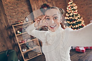 Photo of young cheerful girl happy positive smile show peace cool v-sign make video christmas tree decor lights indoors