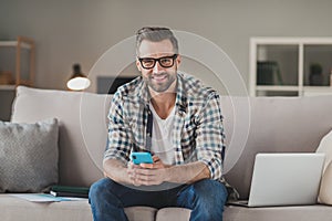 Photo of young cheerful handsome man happy positive smile sit sofa indoors chat type sms browse cellphone