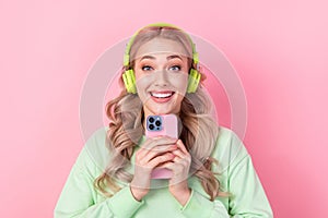 Photo of young excited girlfriend wear green jumper holding apple phone listen bluetooth modern earphones isolated on