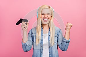 Photo of young excited lady rejoice victory play game listen headphones isolated over pink color background