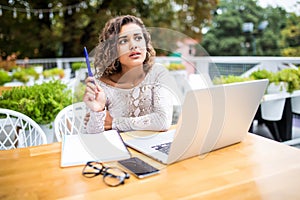 Photo of young excited latin curly woman indoors using laptop computer writing notes Looking aside have an idea in cafe