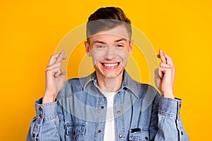 Photo of young excited man crossed fingers wait wish luck pleading isolated over yellow color background