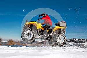 Photo of young extremal driver in red warm winter clothes and black helmet jump in the air with the ATV 4wd quad bike