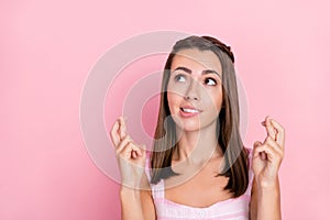 Photo of young girl crossed fingers bite lips anxious wish beg luck success look empty space isolated over pink color