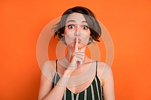 Photo of young girl finger cover lips shh keep secret confidential private isolated over orange color background