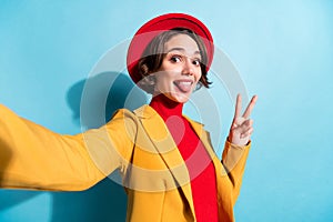 Photo of young girl happy positive smile make selfie grimace tongue-out show peace v-sign isolated over blue color