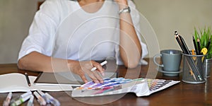 Photo of young graphic designer holding a stylus pen while selecting color from color guide .