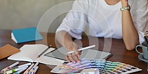 Photo of young graphic designer holding a stylus pen while selecting color from color guide.