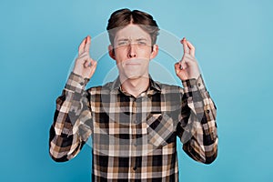 Photo of young guy worried nervous crossed fingers beg wish luck success isolated on blue color background