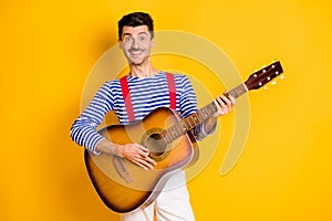 Photo of young handsome funky funny happy smiling cheerful man playing guitar isolated on yellow color background