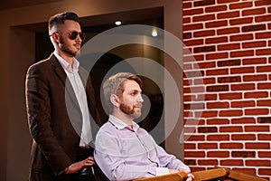 Photo of young handsome man who sitting in chair at barbershop with hairdresses who standing by the armchair photo