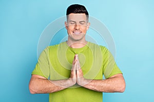 Photo of young happy calm man smile good mood hold hands together pray wish isolated on blue color background