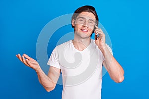 Photo of young happy positive charming man wear glasses talk hold phone smile isolated on blue color background