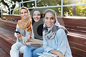 Photo of young islamic women wearing headscarfs sitting on bench in park