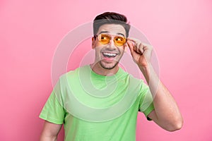 Photo of young macho smiling guy trying new sunglasses oakley wearing green t shirt looks empty space isolated on pink