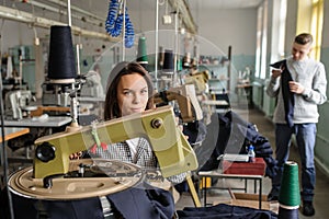 photo of a young man analysing a piece of work and a woman working with linking machine for knitting in textile industry