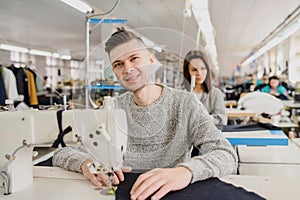 Photo of a young man and other seamstresses sewing with sewing machine in a factory