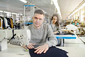 photo of a young man and other seamstresses sewing with sewing machine in a factory