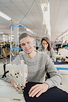 Photo of a young man and other seamstresses sewing with sewing machine in a factory