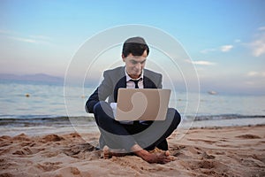 photo of a young man in suit with laptop working on the beach and talking to someone