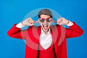 Photo of young man unhappy angry mad cover fingers ears loud noise mad isolated over blue color background