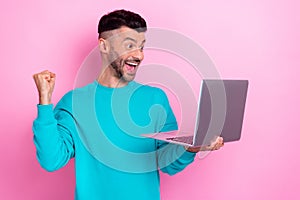 Photo of young overjoyed attractive guy wear blue sweatshirt raise fist up hold netbook celebrate online bet win