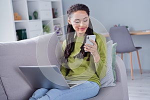 Photo of young peaceful woman sit sofa look phone laptop weekend indoors inside house home flat