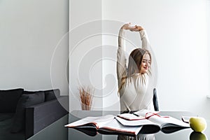 Photo of young pleased woman stretching her body while sitting