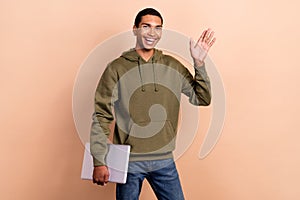 Photo of young positive cheerful guy wear khaki hoodie shake palm hello people hold netbook friendly office work