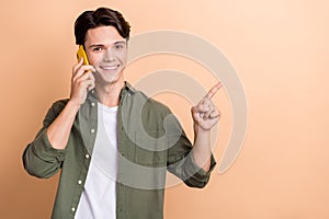 Photo of young positive student man brunet hair wear khaki trendy shirt talking phone point finger empty space isolated