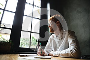 Photo of young smiling handsome readhead bearded man sitting on