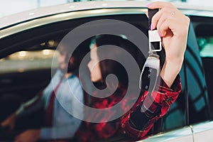 Photo of young smiling mixed race woman sitting inside her new car and holding key. Concept for car rental.