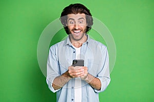 Photo of young stubbled guy hold smartphone amazed crazy face wear jeans shirt isolated green color background photo