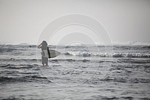 Photo of young surfer with surf board. Man standing in the sea and looking waves. Ready for surfing. Horizontal