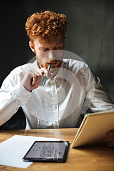 Photo of young thinking readhead bearded man in white shirt