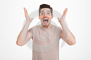 Photo of young unshaved guy with exciting facial expressions shouting and gesturing with hands in happiness and