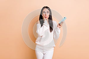 Photo of young woman amazed shocked surprised news fake novelty use smartphone isolated over beige color background