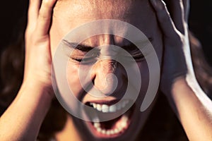 A young woman close-up screaming on black background. Mental illness concept