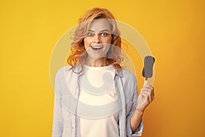 Photo of young woman eats delicious ice cream, enjoys frozen dessert, dressed in casual clothes, isolated on yellow