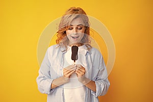Photo of young woman eats delicious ice cream, enjoys frozen dessert, dressed in casual clothes,  on yellow