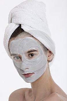 Portrait of young woman with face pack and towel wrapped around head against white background