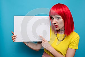 Photo of a young woman. Happy positive smile, index finger pointing to the empty space of a poster or promotional ad.