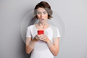 Photo of young woman hold cellphone amazed shocked surprised bad comment news isolated over grey color background